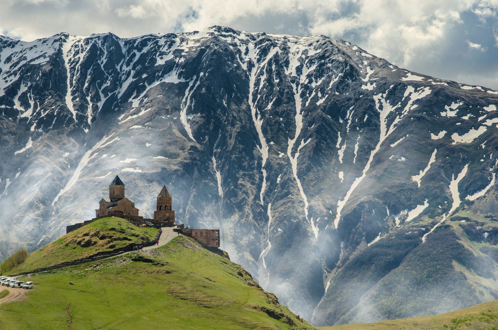 Gergeti-Dreifaltigkeitskirche auf einem grünen Hügel vor einem schneebedeckten Berg in Georgien