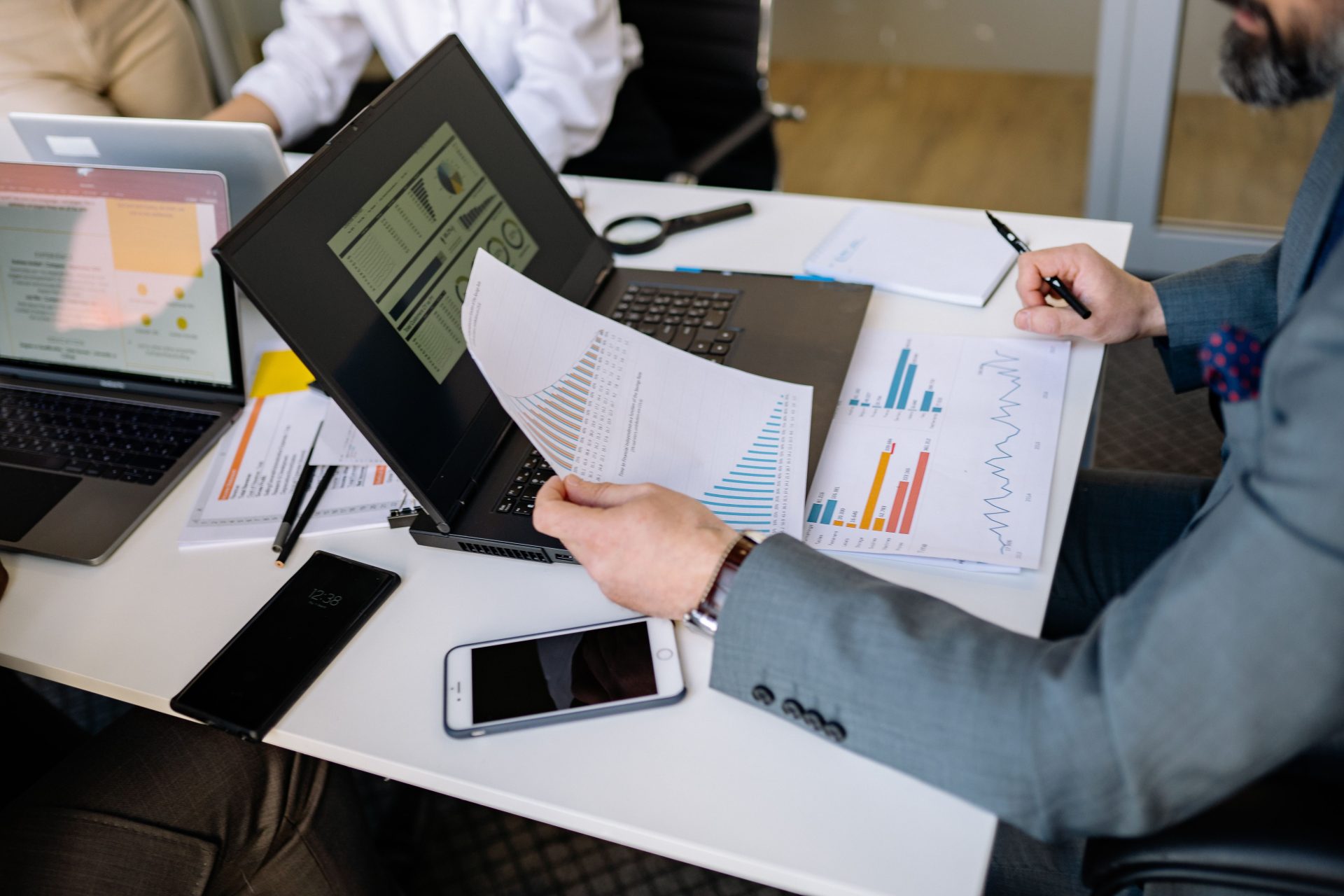 Fachleute analysieren während einer geschäftlichen Besprechung Diagramme und Grafiken auf Laptops.